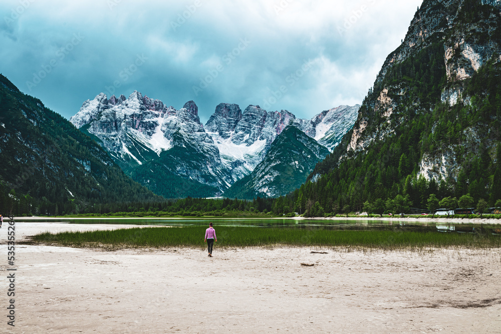 Young woman walks at sand beach during a rainy noon. Dürrensee (Lago di Landro), Saint Ulrich, Dolomites, Belluno, Italy, Europe.