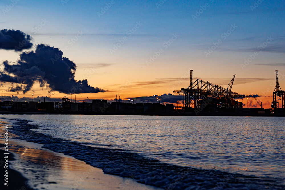 Panoramic image of the cargo port at sunset. Gdansk at night with container terminals, cargo cranes at sea and clear blue sky. Cargo sea port