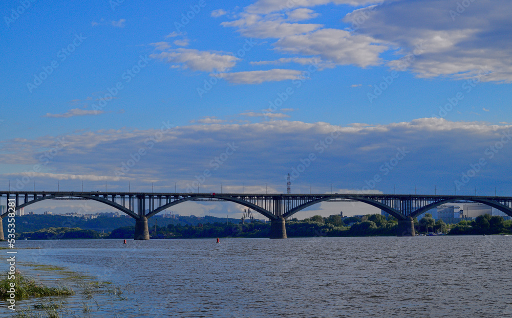A bridge, a wide river and a blue sky with clouds. A multi-span bridge over a large river. A landscape with a bridge over a river and a beautiful sky.