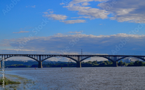 A bridge  a wide river and a blue sky with clouds. A multi-span bridge over a large river. A landscape with a bridge over a river and a beautiful sky.
