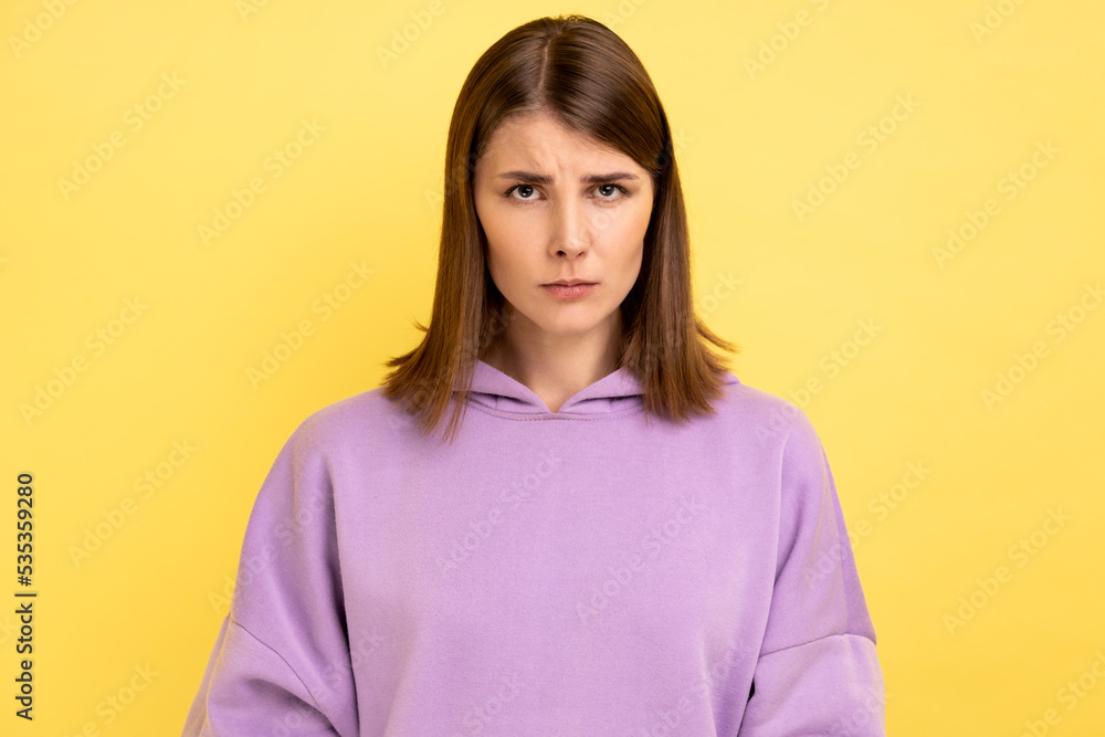 Portrait of disappointed woman being upset of bad news, looking at camera with frowning face, expressing sadness, wearing purple hoodie. Indoor studio shot isolated on yellow background. Portrait of disappointed woman being upset of bad news, looking at camera with frowning face, expressing sadness, wearing purple hoodie. Indoor studio shot isolated on yellow background.