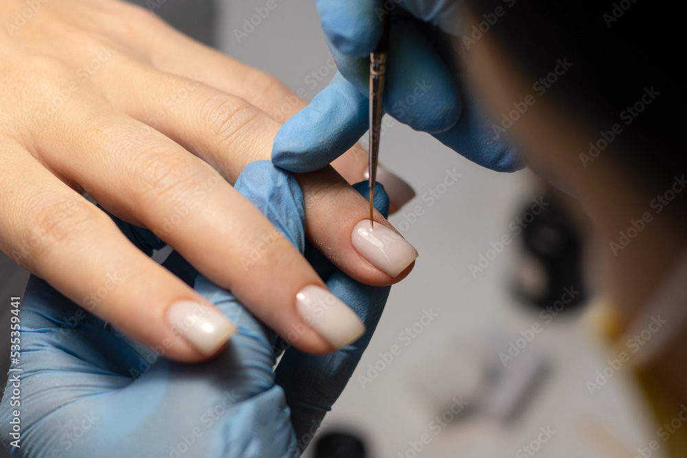 The process of doing a manicure in a spa salon. Manicurist applies milky gel polish on nails in a beauty salon. Applying gel polish. Hand care concept.