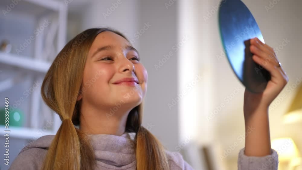 Smiling satisfied teen girl admiring reflection in hand mirror sitting at home indoors. Portrait of happy confident Caucasian teenager with ponytails getting ready in the morning. Beauty and lifestyle Smiling satisfied teen girl admiring reflection in hand mirror sitting at home indoors. Portrait of happy confident Caucasian teenager with ponytails getting ready in the morning. Beauty and lifestyle