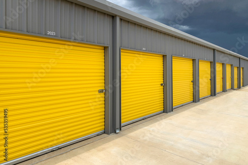 Fotografering Exterior of a commercial warehouse with yellow roller doors, garages, self stora