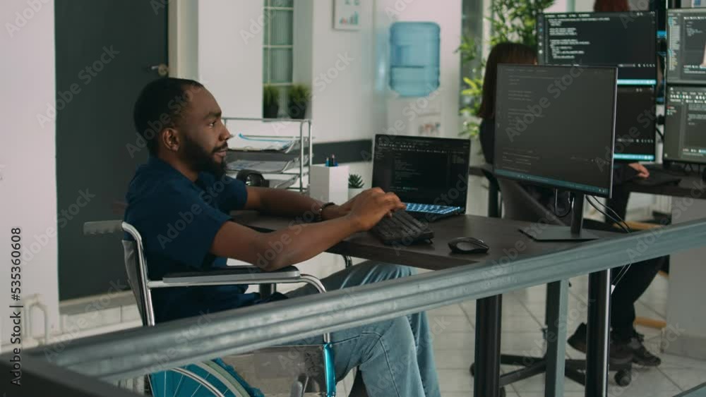 Wheelchair user software engineer working on server program with computer, typing in it coding office. Database programer with chronic disability writing code with system algorithms. Wheelchair user software engineer working on server program with computer, typing in it coding office. Database programer with chronic disability writing code with system algorithms.