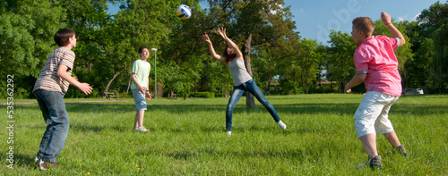 Teenagers boys and girls playing volleyball in the park on sunny spring day