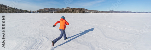 Woman running on frozen lake in snowy winter nature landscape. Winter fun in snow. Panoramic banner