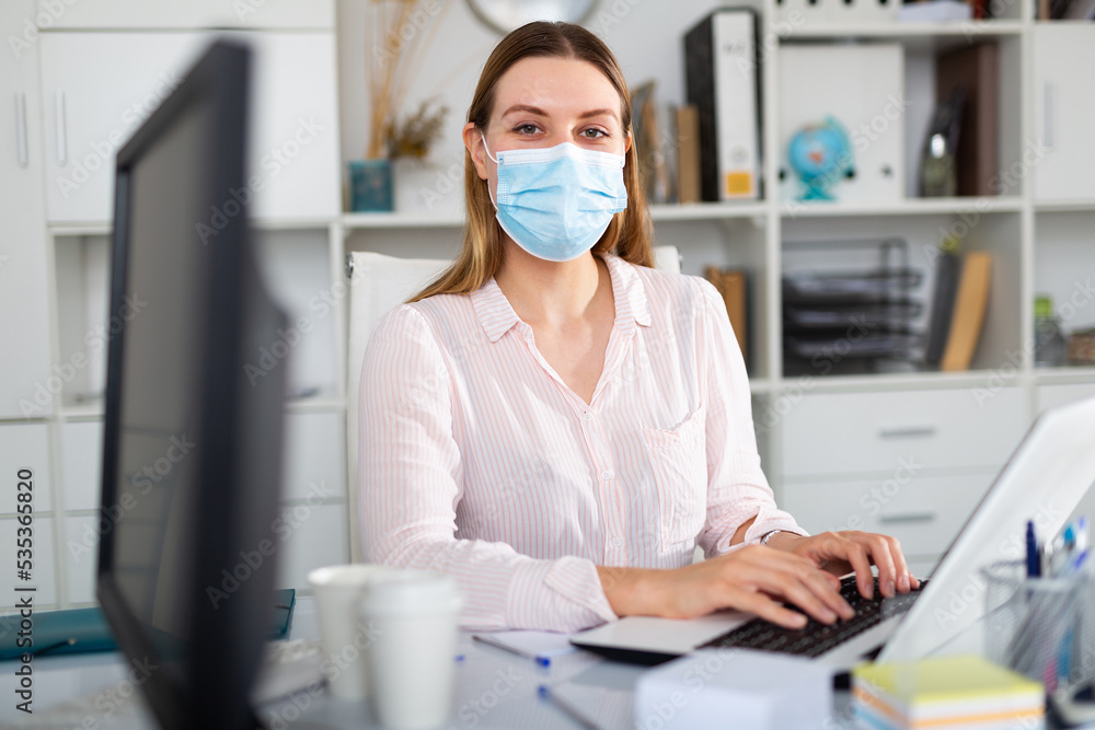 Businesswoman in personal protective equipment working on laptop in office