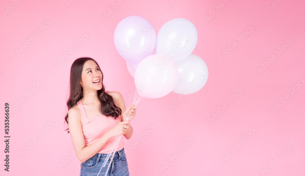 Excited cheerful asian woman holding balloons and hands beside mouth smiling with toothy standing over isolated pink background. Joyful teenager girl with pastel balloons shocked amazed expression. Excited cheerful asian woman holding balloons and hands beside mouth smiling with toothy standing over isolated pink background. Joyful teenager girl with pastel balloons shocked amazed expression.