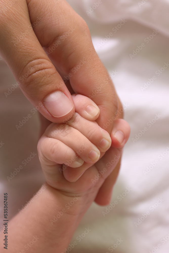 Mother and her newborn baby on bed, closeup of hands Mother and her newborn baby on bed, closeup of hands