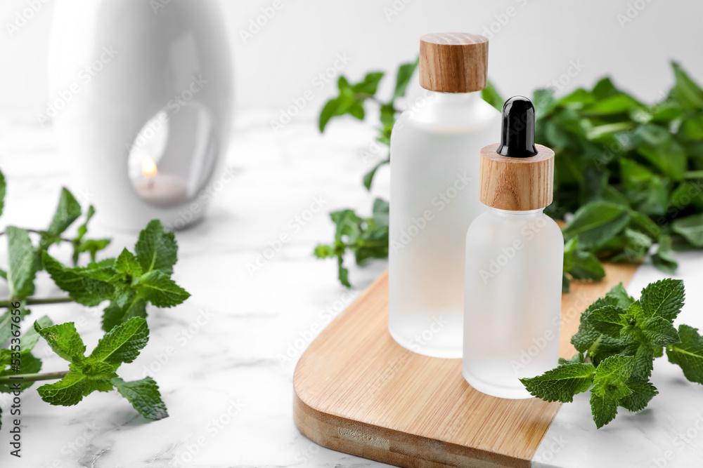 Bottles of mint essential oil and fresh leaves on white marble table Bottles of mint essential oil and fresh leaves on white marble table