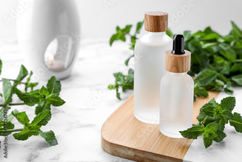 Bottles of mint essential oil and fresh leaves on white marble table