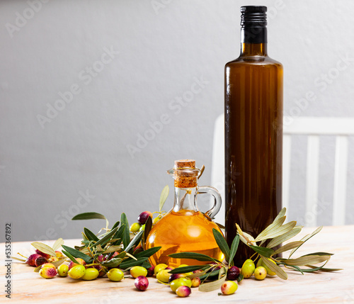 Glass bottles and carafes with fresh olive oil on wooden table with olive branches and fresh olives. High quality photo