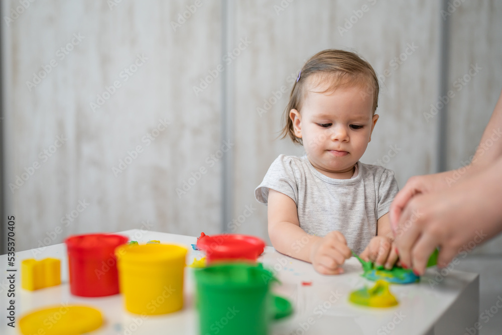 One girl small caucasian toddler child playing with colorful plasticine on the table at home alone childhood and growing up development concept copy space One girl small caucasian toddler child playing with colorful plasticine on the table at home alone childhood and growing up development concept copy space