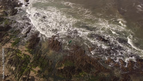 Aerial shot of Surfer with Surfboard entering Atlantic Ocean for surfing during large waves - Walking between rocks and stones at shoreline