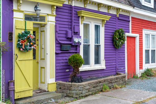 St. John's, Newfoundland, Canada - October 2022:Purple and red colored row houses with an attached and shared common red door. Both houses have Christmas wreaths and windows hanging on the wooden wall photo