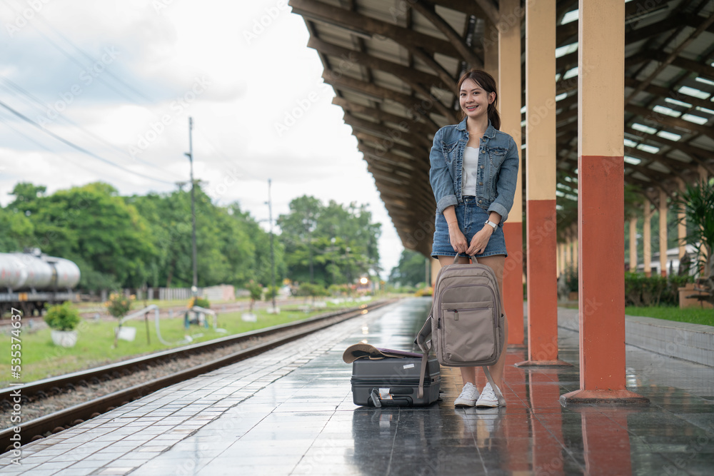 Asian female traveler with suitcase standing on a platform of railroad station while waiting for the train.