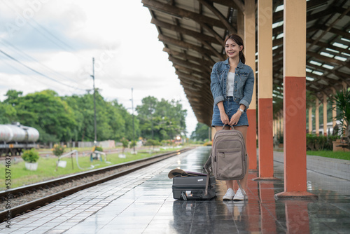 Asian female traveler with suitcase standing on a platform of railroad station while waiting for the train.
