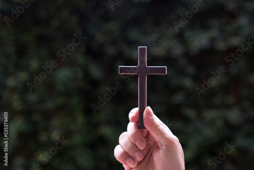 Hand holding a wooden cross crucifix with nature background. Concept for Christian faith and Good Friday.