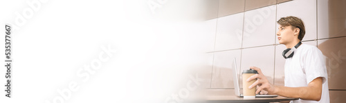 guy student sits at a table outdoor with laptop and coffee. Selective focus, banner