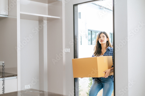 Young woman carry large package walk into new house