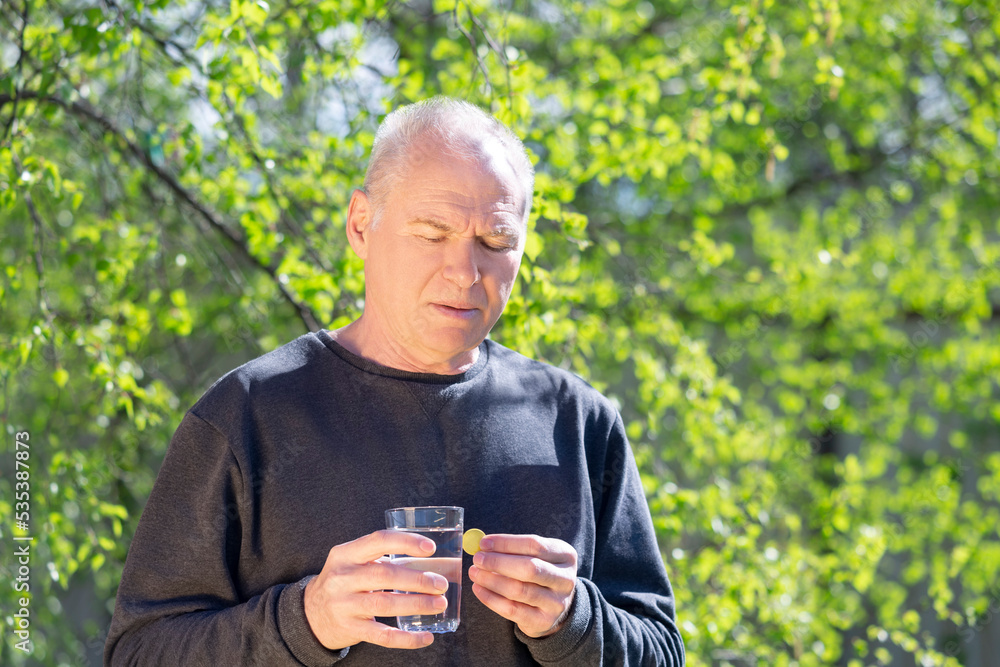 A man with a soluble effervescent tablet and a glass of water against the background of spring foliage A man with a soluble effervescent tablet and a glass of water against the background of spring foliage