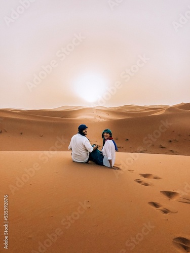 Man and woman sitting on sand dune in desert in Errachidia, Morocco photo
