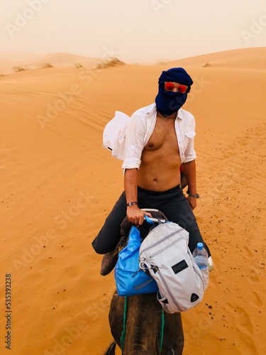 Man wearing shemagh riding a camel in desert photo
