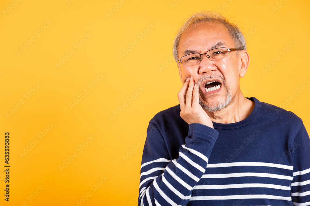Dental pain. Asian unhappy elder man problems with gum pain studio shot isolated on yellow background, Portrait senior old man sad hand touching cheek suffering from toothache, dental healthcare Dental pain. Asian unhappy elder man problems with gum pain studio shot isolated on yellow background, Portrait senior old man sad hand touching cheek suffering from toothache, dental healthcare