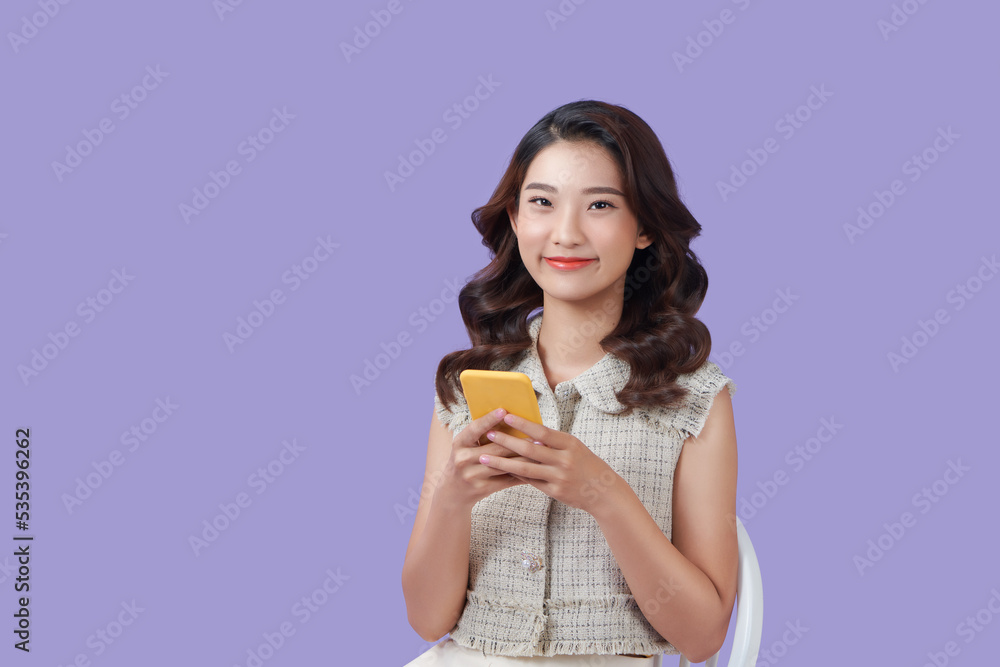 Asian woman sitting on sofa using her phone with a happy expression Asian woman sitting on sofa using her phone with a happy expression