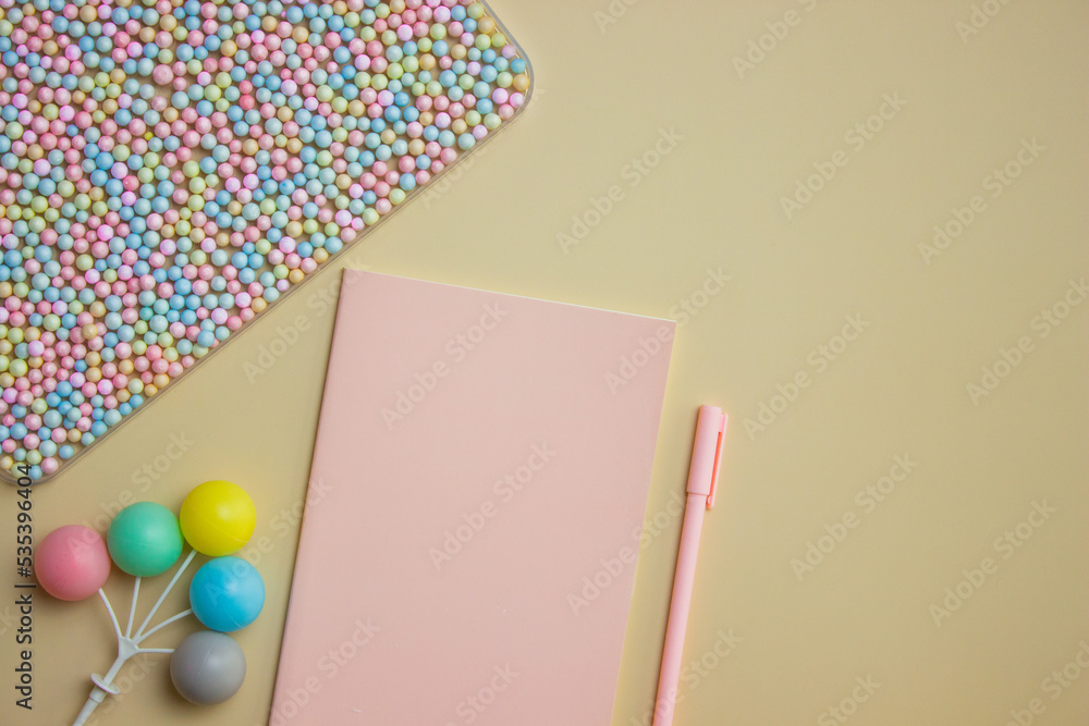 Colorful small balls with pink notebook and pen over the brown background. Colorful small balls with pink notebook and pen over the brown background.