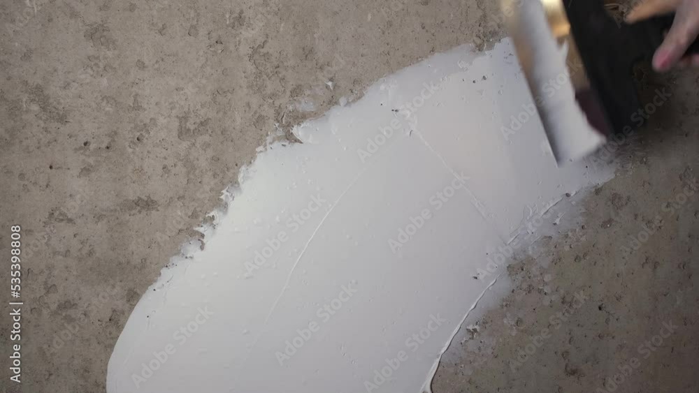 Puttying process. A female gloved hand works with a concrete wall. White putty lays evenly on the surface of the wall Puttying process. A female gloved hand works with a concrete wall. White putty lays evenly on the surface of the wall