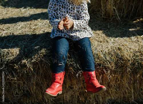 little girl in red cowgirl boots sitting on a hay bale at a farm