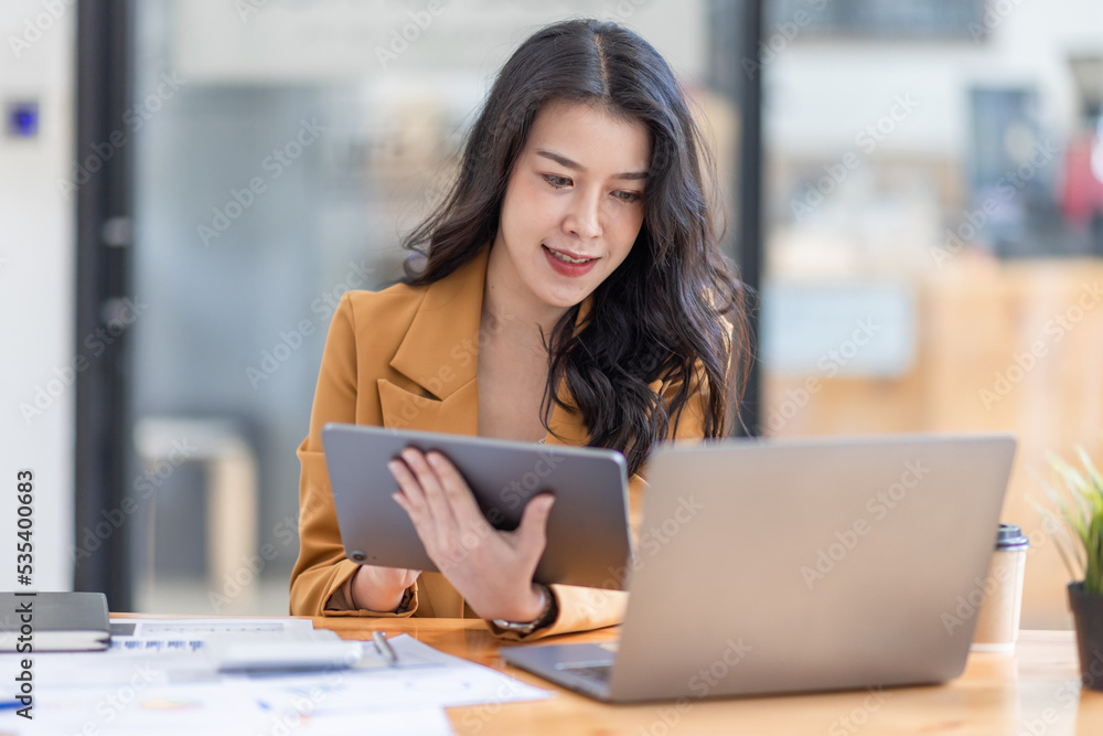 © David - Asian businesswoman working in the  workplace Office, Her is using touchpad while reading an e-mail on laptop and taking notes on the paper, accounting, tax, Financial, Business concept