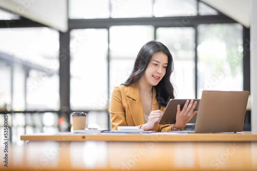 Asian businesswoman working in the  workplace Office, Her is using touchpad while reading an e-mail on laptop and taking notes on the paper, accounting, tax, Financial, Business concept