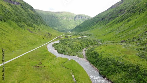 Car passing on straight lined road in beautiful serene idyllic and lush green valley with river at Vikafjell mountain close to Voss Norway - Aerial moving forward and sideways towards road rv13 photo