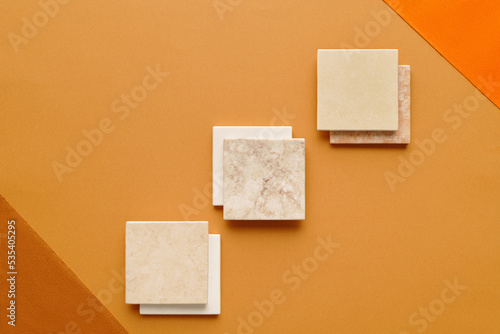 Horizontal top-down minimalistic flat lay shot of square ceramic tiles on light brown and orange surface photo