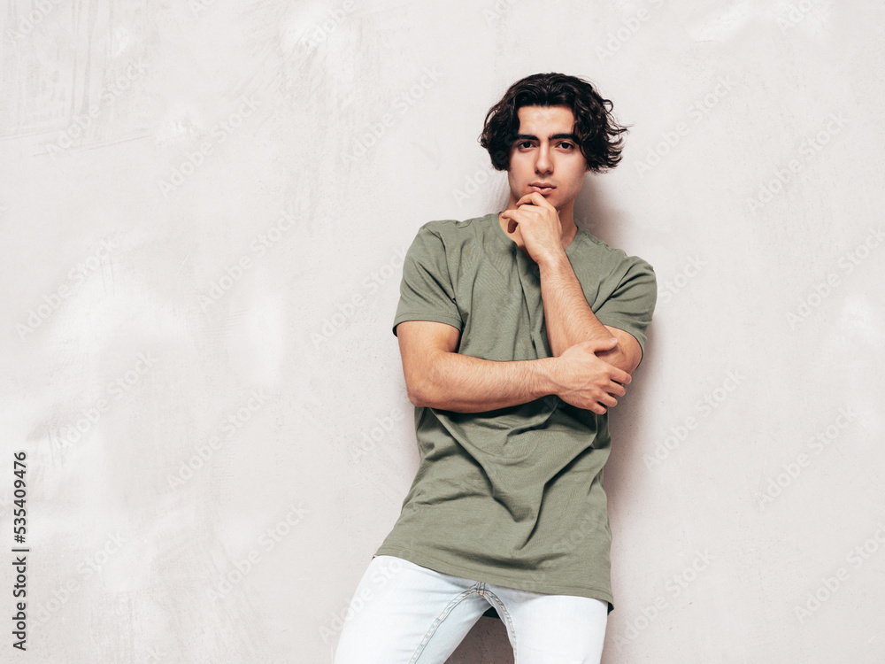 Portrait of handsome confident stylish hipster lambersexual model.Man dressed in over size T-shirt and jeans. Fashion male isolated in studio. Posing near grey wall Portrait of handsome confident stylish hipster lambersexual model.Man dressed in over size T-shirt and jeans. Fashion male isolated in studio. Posing near grey wall