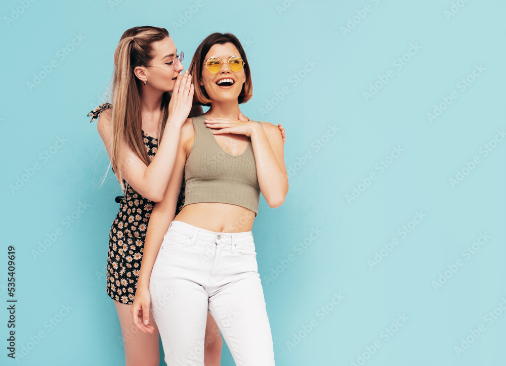Two young beautiful smiling brunette hipster female in trendy summer clothes. Sexy carefree women posing near blue wall. Positive models having fun. Tells secret. Shocked and surprised Two young beautiful smiling brunette hipster female in trendy summer clothes. Sexy carefree women posing near blue wall. Positive models having fun. Tells secret. Shocked and surprised