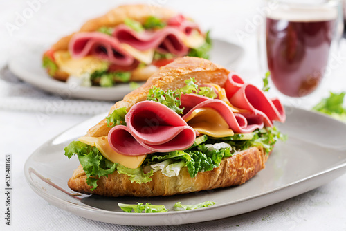 Fresh croissant or sandwich with salad, ham and cheese on light background.