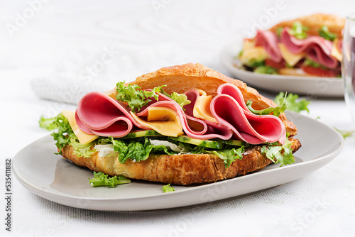 Fresh croissant or sandwich with salad, ham and cheese on light  background.
