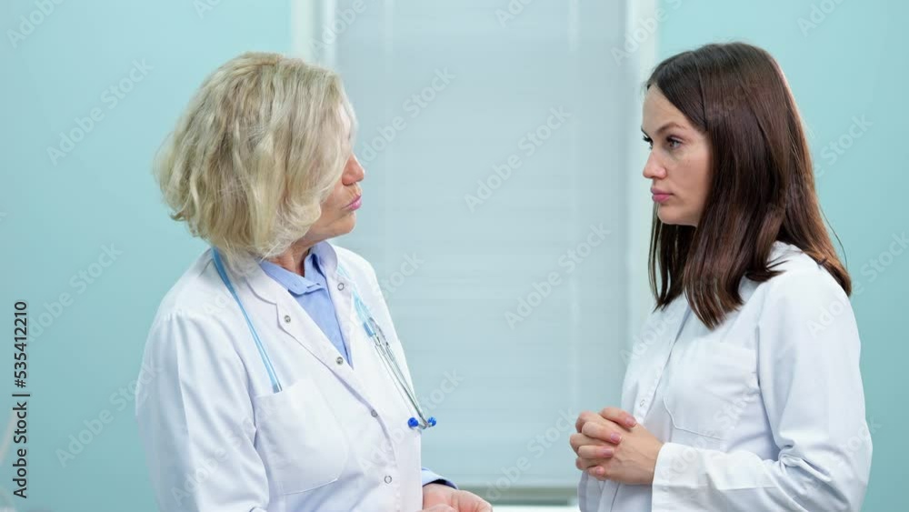 Encouraging couple of doctors advise on treatment of new patients in waiting room. Brunette lady tells about new method of medicating cardiovascular disease Encouraging couple of doctors advise on treatment of new patients in waiting room. Brunette lady tells about new method of medicating cardiovascular disease