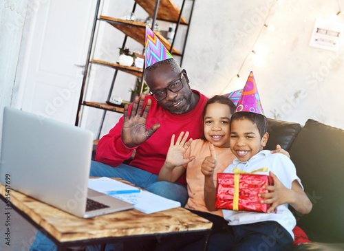 family - dad, daughter and son in festive hats celebrate birthday, smile and communicate with relatives via video link.