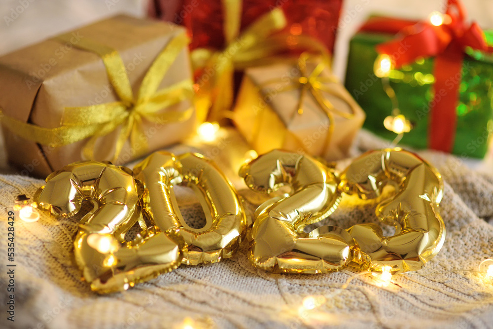 golden numbers 2023 on a knitted plaid on the background of Christmas gifts and Christmas lights. golden numbers 2023 on a knitted plaid on the background of Christmas gifts and Christmas lights.