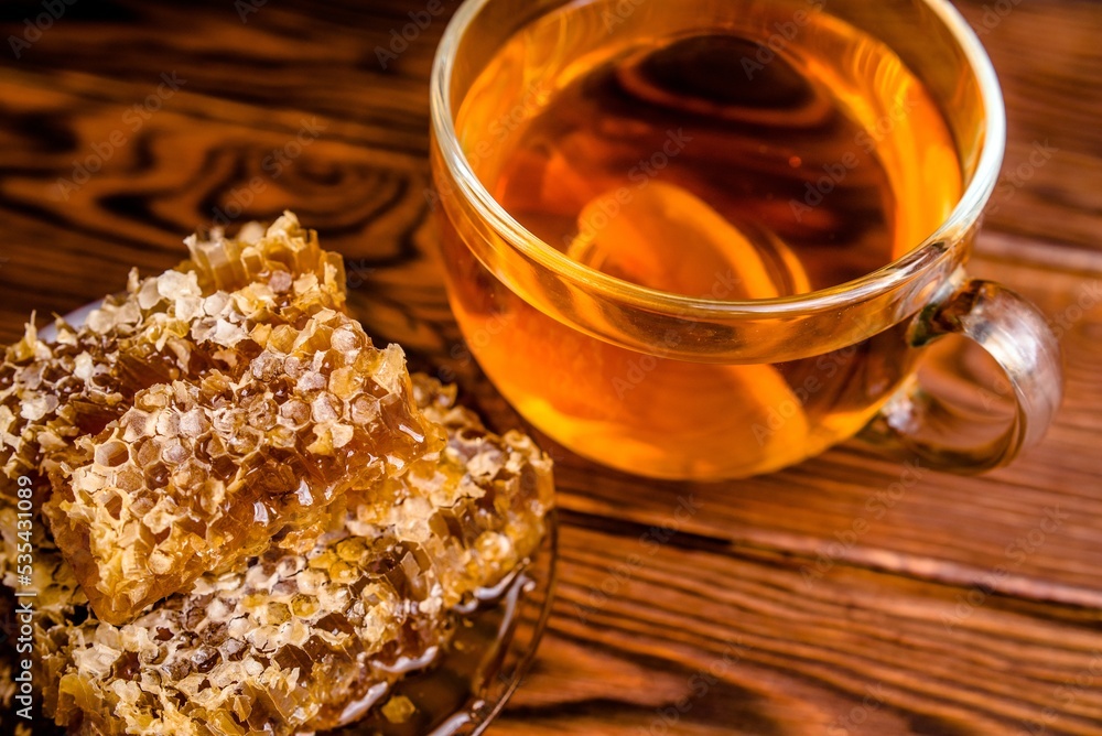 honey in honeycombs and a mug of tea on a brown wooden background honey in honeycombs and a mug of tea on a brown wooden background