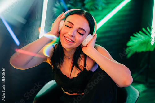 Fashion pretty woman with headphones listening to music over neon background at studio.