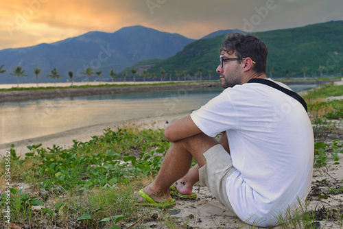 Upset man sitting at beach and watching sunset in tropics of Vietnam