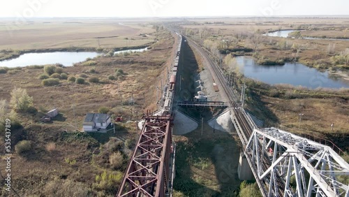 An electric locomotive with freight cars with coal travels by rail on a railway bridge across the river. Transportation and delivery of goods in wagons.Transportation and logistics on the railway.