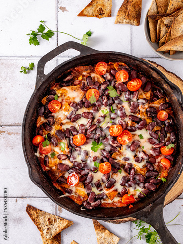 Mexican vegetarian dish with tortillas in an iron skillet on tiles, breakfast idea with black beans, cherry tomatoes, tortillas, and cheese, top view