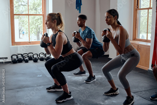 Three determined multiracial young adults doing kettlebell squats at the gym